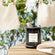 Photo shot of a Roesia - Breezy Linen 10oz candle placed on a table by the lake, with clothes hanging by the lakeside