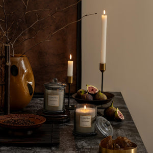  Photo shot of lit Roesia - Santal Himalayen 10oz candles placed on a marble table, surrounded by figs, candleholders, and a vase
