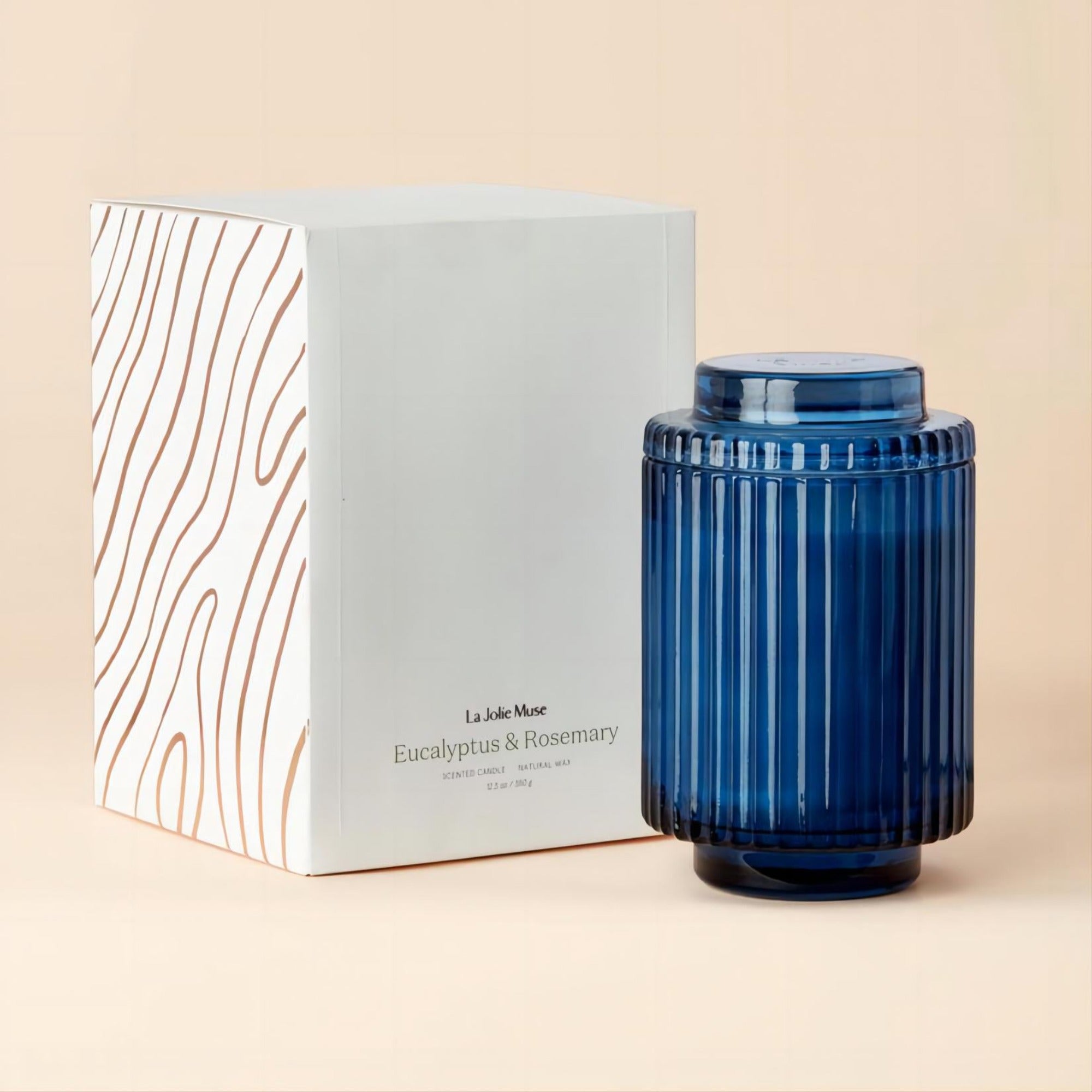 Photo shot of Amélie - Eucalyptus & Rosemary 12.3oz candle positioned on the right side of a plain background, with its outer packaging box placed to the left
