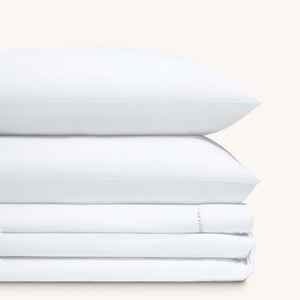 Camille Classic White bed sheet set. Two white pillows stacked on folded white sheet set.