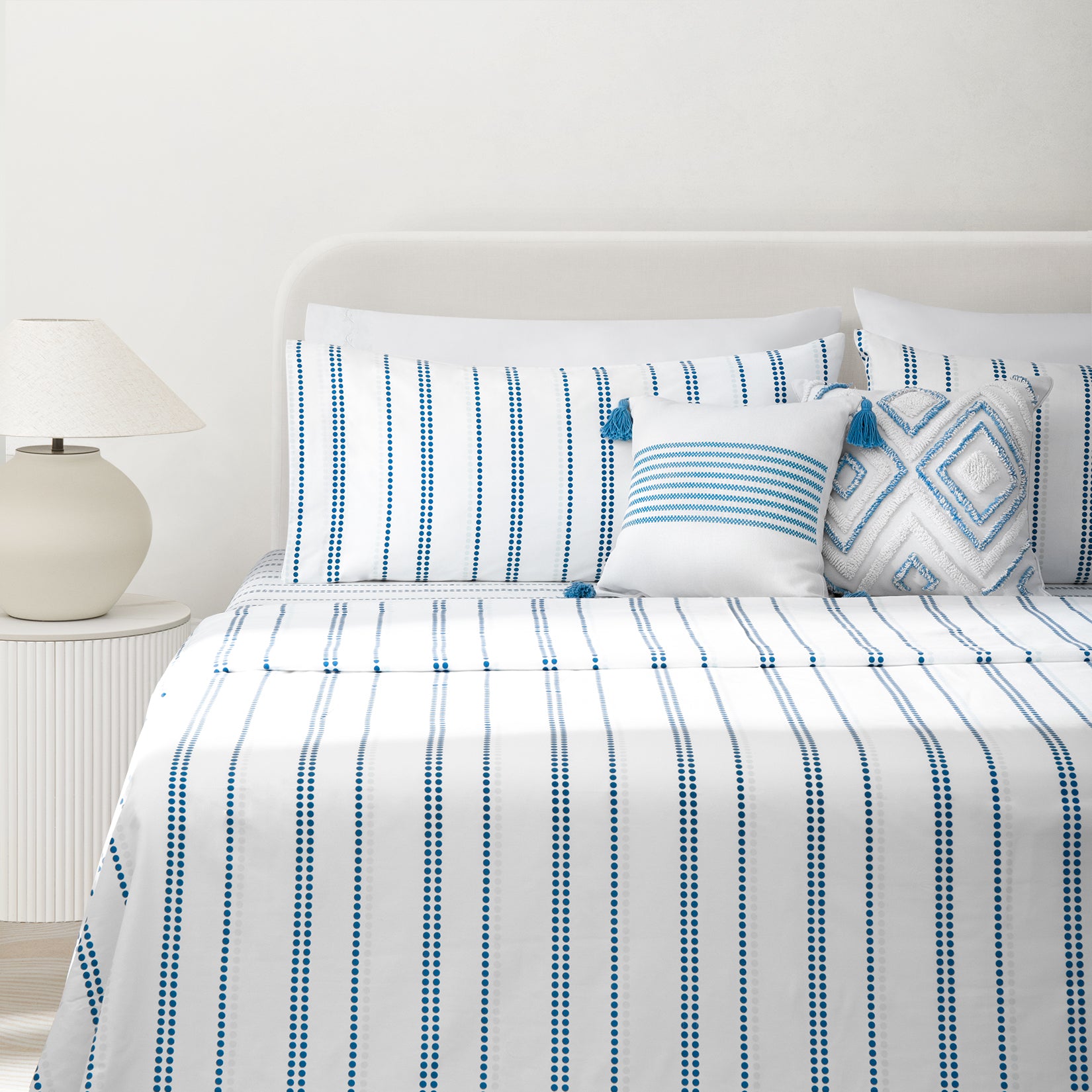 Camille Blue stripe bed sheets set. Dotted blue and white bedding set with striped accent pillow with tassles and tufted diamond accent pillow on bed and bedside lamp.