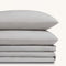 Paulina Foggy Triple Satin Stitched Cuff 200 thread count cotton bed sheet set. Two gray pillows stacked on folded gray sheet set.