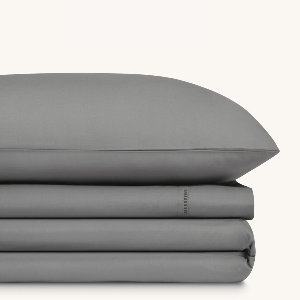 Camille Mid Gray bed sheet set. Single dark gray pillow stacked on folded dark gray sheet set.