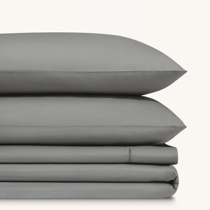Camille Mid Gray bed sheet set. Two dark gray pillows stacked on folded dark gray sheet set.