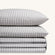 Paulina Pewter Check Picot Edge 200 thread count cotton bed sheet set. Two white and gray gingham pillows stacked on folded white and gray gingham sheet set.