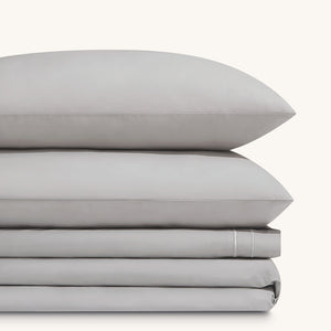 Sofia Foggy Gray Double Satin Stitched Cuff 300 thread count cotton bed sheet set. Two gray pillows stacked on folded gray sheet set.