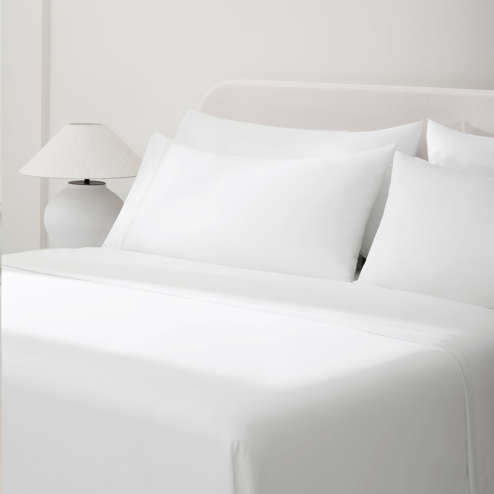 Camille Classic White Pleated bed set. White pillows and white sheets on bed with side table and lamp from side angle.