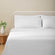 Nina Classic White 600 thread count sheet set on a fully made bed. White embroidered duvet and four white embroidered pillows next to side table with plant.