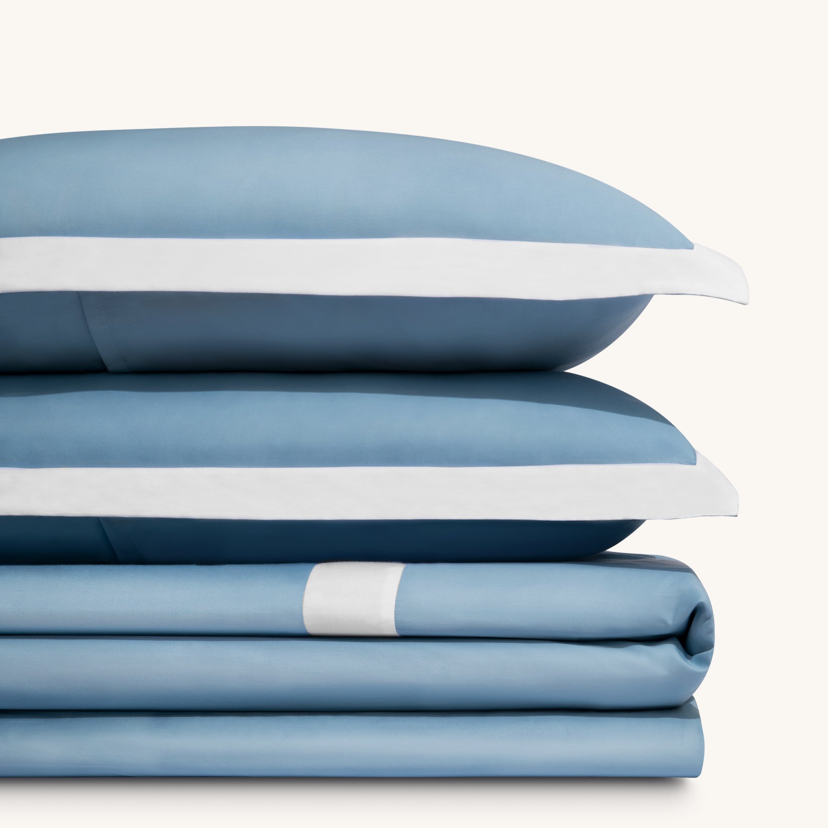 Paulina Sky Blue 200 thread count combed cotton duvet set. Two white and sky blue pillows stacked on folded white and blue cotton duvet set.Paulina Sky Blue 200 thread count combed cotton duvet set. Two white and sky blue pillows stacked on folded white and blue cotton duvet set.