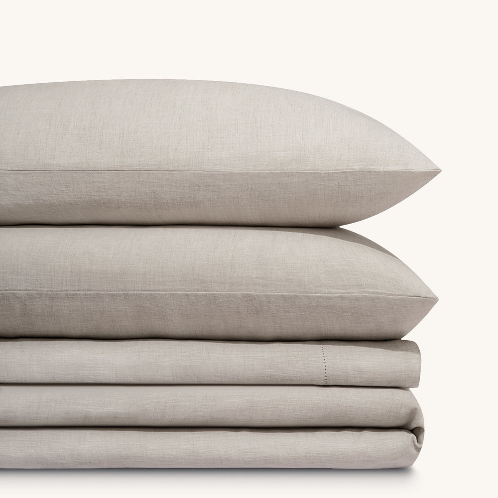 Olivia natural taupe linen bed sheet set. Two natural taupe  linen pillows stacked on folded natural taupe linen sheet set.