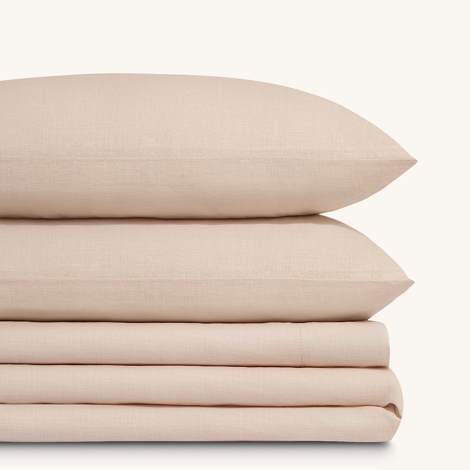 Olivia Blush linen bed sheet set. Two blush pink linen pillows stacked on folded blush pink linen sheet set.