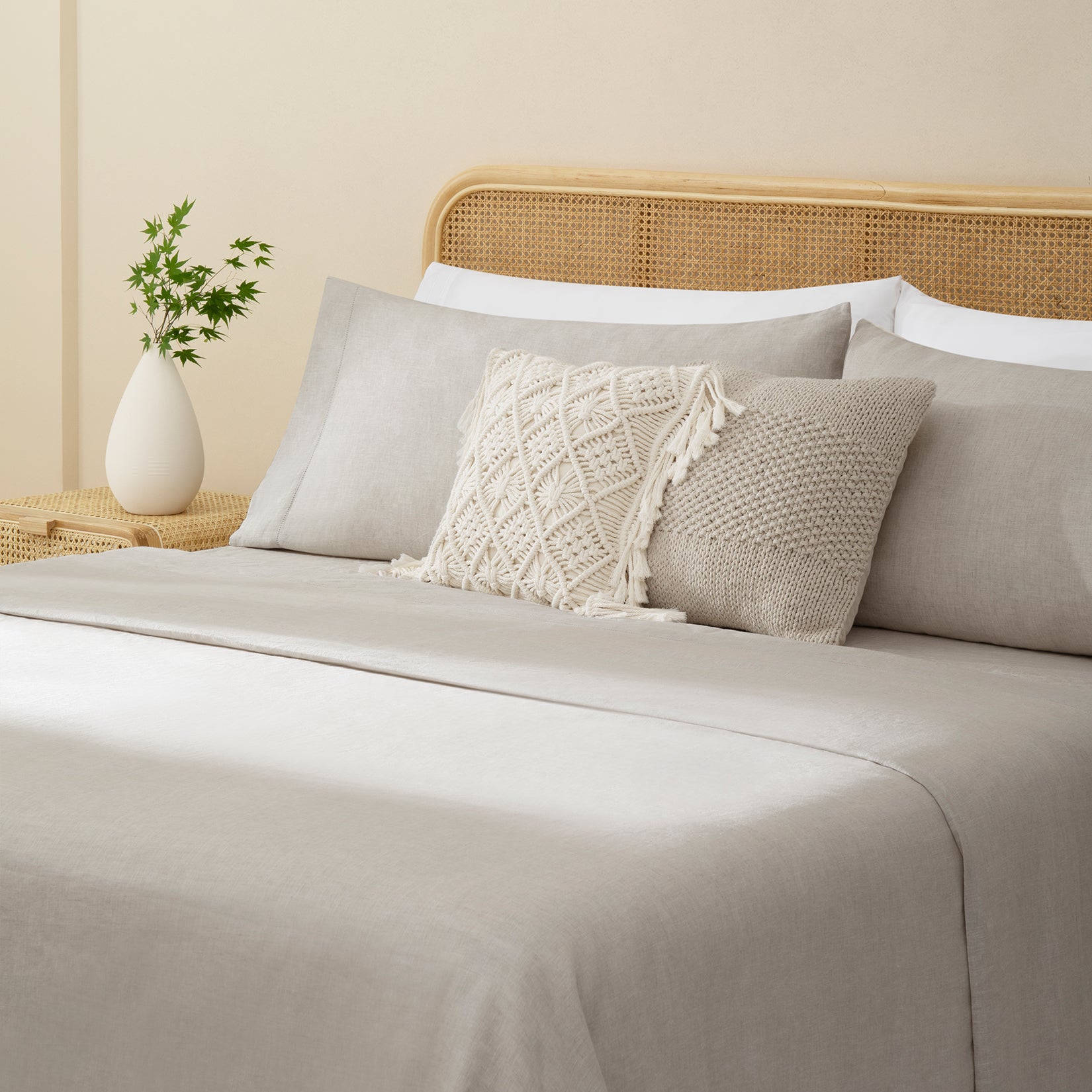 Olivia natural taupe linen sheet set. Natural taupelinen pillows and natural taupe duvet on bed with plant on side table from side angle.