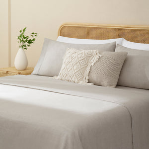 Olivia natural taupe linen sheet set. Natural taupelinen pillows and natural taupe duvet on bed with plant on side table from side angle.