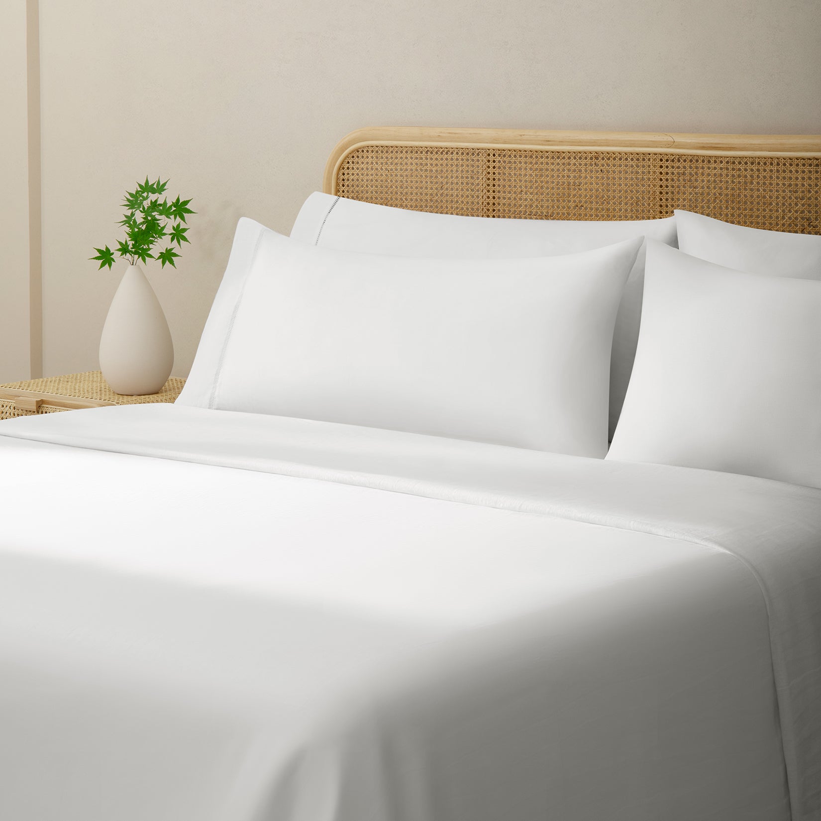 Olivia soft white linen sheet set. Soft white linen pillows and soft white duvet on bed with plant on side table from side angle.