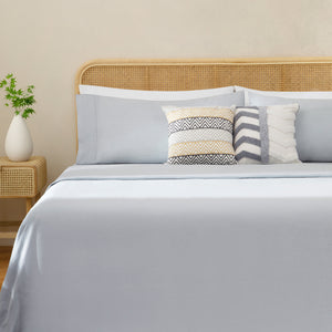 Olivia foggy gray linen sheet set on a fully made bed next to side table with plant and accent pillows. Foggy gray duvet with two white pillows, two foggy gray pillows.