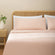 Olivia blush pink linen sheet set on a fully made bed next to side table with plant. Blush pink duvet with two white pillows, two blush pink pillows.