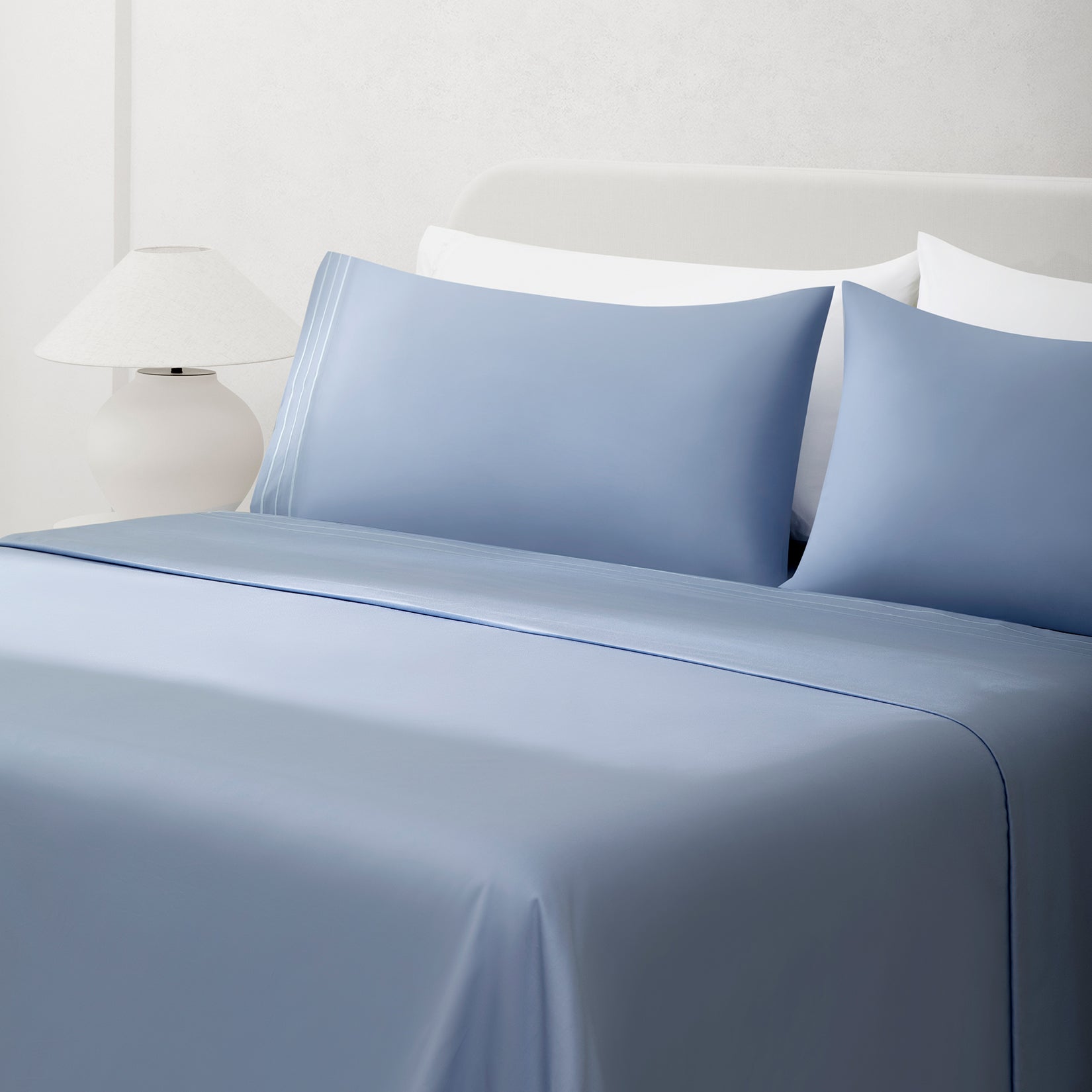 Paulina Sky Blue Satin Stitched Cuff 200 thread count cotton bed sheet set. Sky blue pillows and sky blue cotton sheets on bed next to side table and lamp.