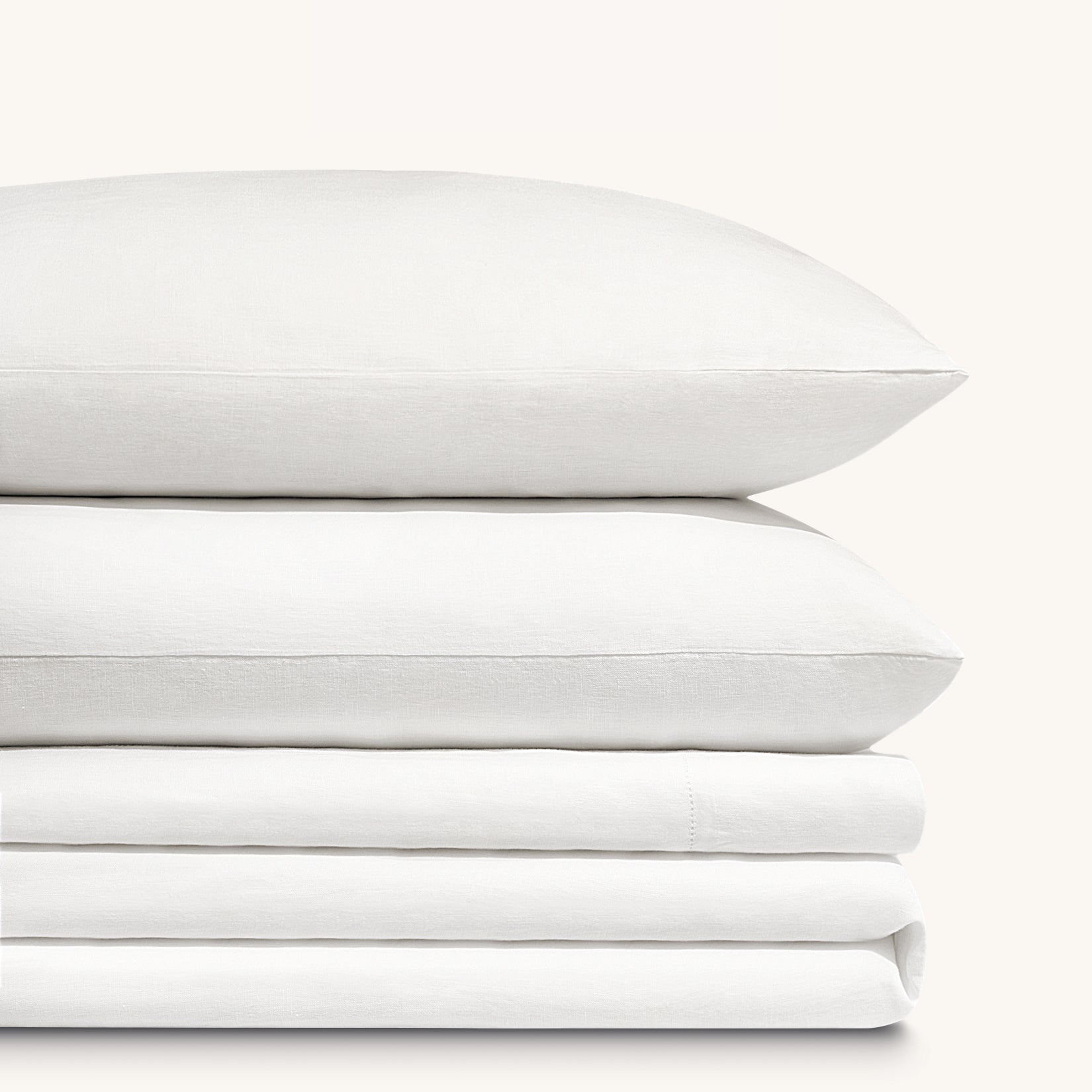 Olivia soft white linen bed sheet set. Two soft white linen pillows stacked on folded soft white linen sheet set.