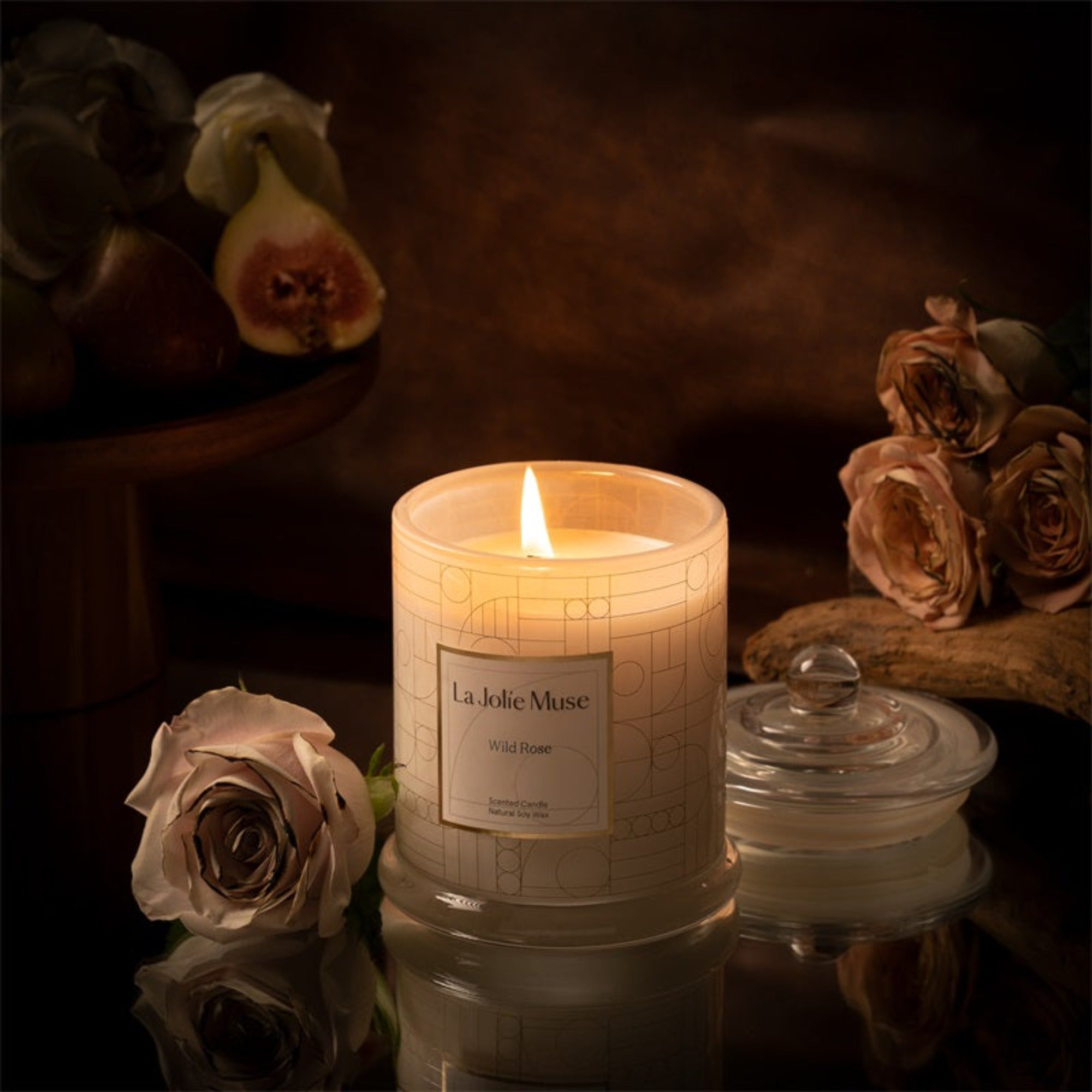 Photo shot of a lit Roesia - Wild Rose 9.9oz candle placed in the middle, surrounded by roses and figs - view 1