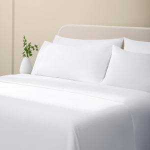 Camille Classic White bed set. White pillows and white dotted sheets on bed with side table and plant from side angle.