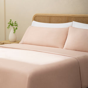 Olivia blush pink linen sheet set. Blush pink linen pillows and blush pink duvet on bed with plant on side table from side angle.