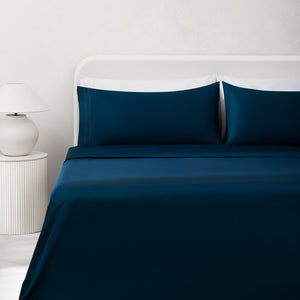 Sofia Navy Blue Double Satin Stitched Cuff 300 thread count cotton bed sheet set on a fully made bed. Navy cotton duvet, navy pillows, next to side table with lamp.