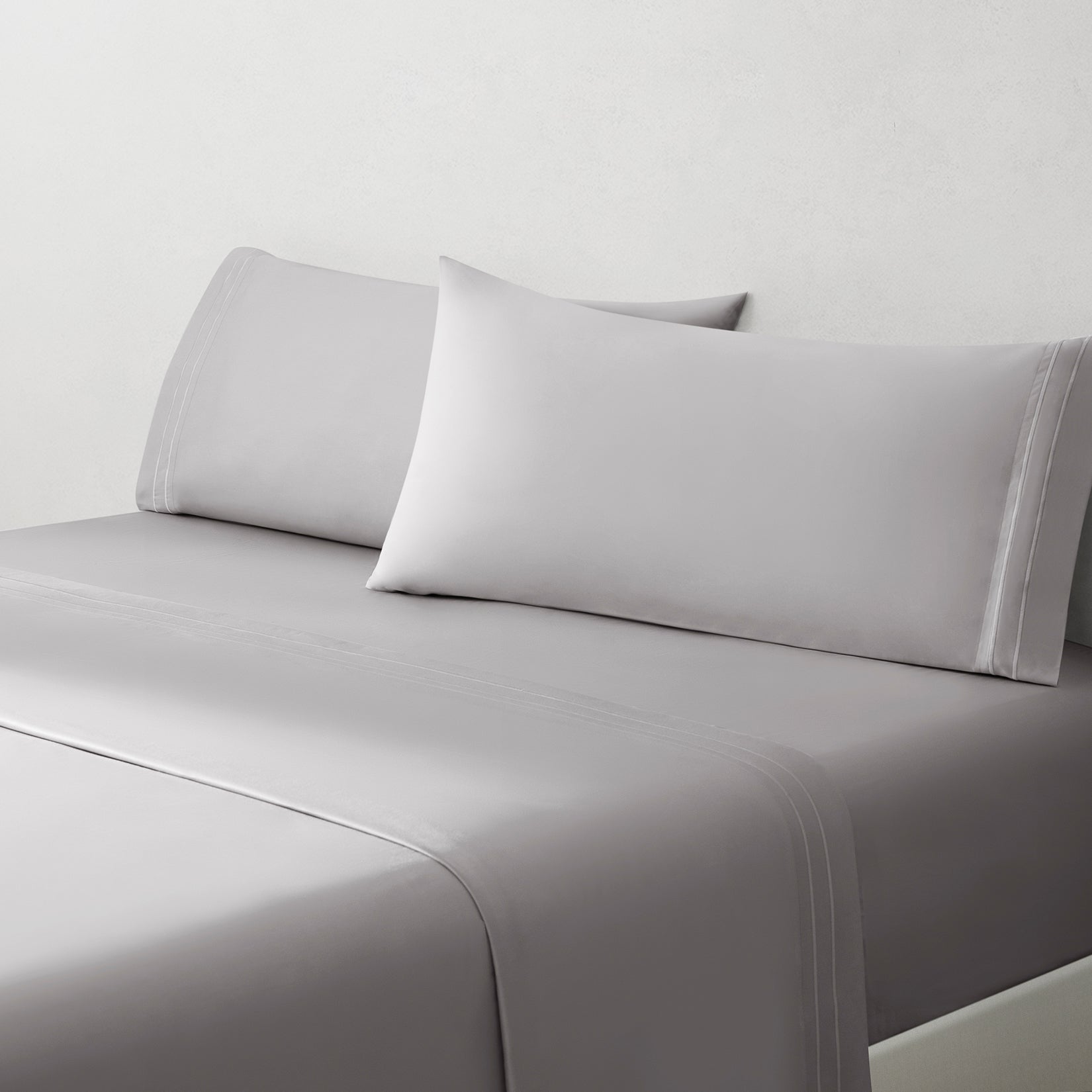 Sofia Foggy Gray Double Satin Stitched Cuff 300 thread count cotton bed sheet set. White pillows and white cotton sheets on bed from side angle.