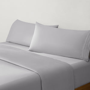 Paulina Foggy Triple Satin Stitched Cuff 200 thread count cotton bed sheet set. Gray pillows and gray cotton sheets on bed from side angle.