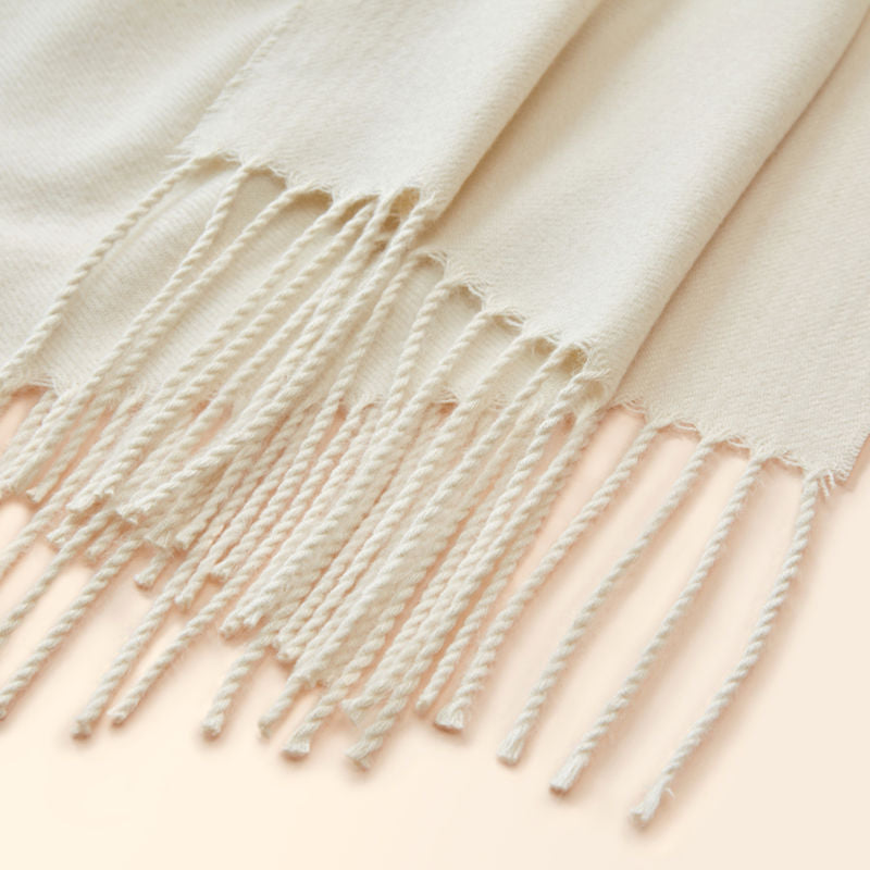 The close-up of the white throw, showing its tassels design and soft rim.