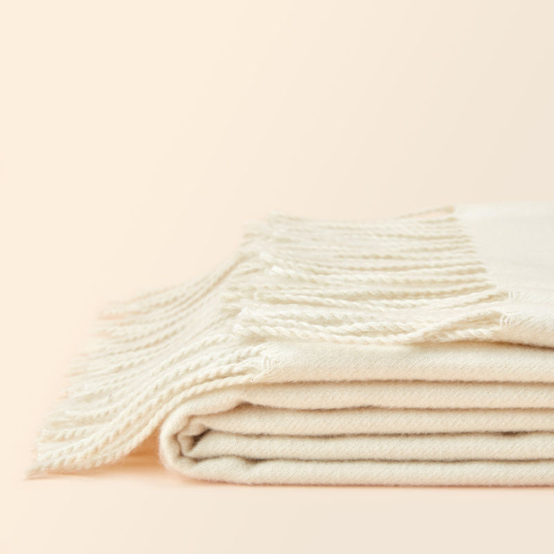 The full view of the Angie cream white throw, which is folded up and shows its tassels.