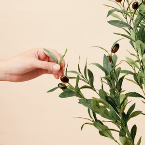 A hand picks the leaves of a plastic olive tree, which has detachable branches.