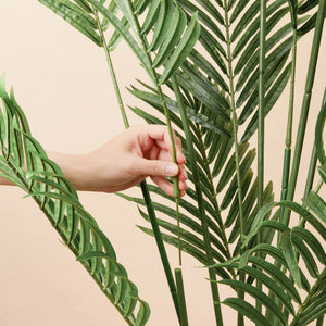 A hand picks a branch of the artificial palm tree and shows the detachable feature.