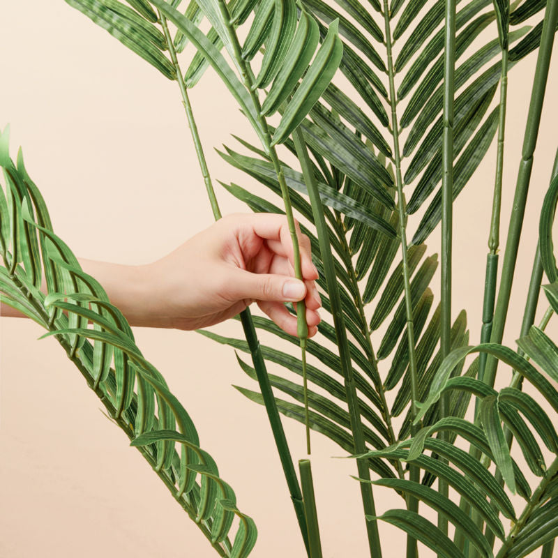 A hand is picking the branch of an artificial palm tree, showing its detachable foliage. 