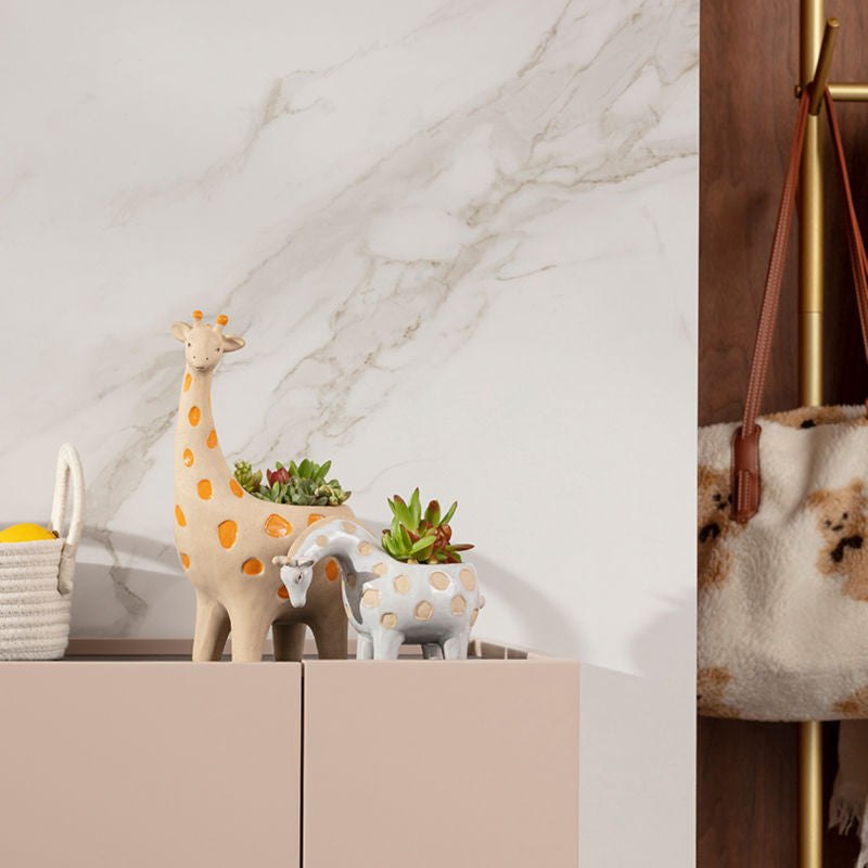 A pair of giraffe pots with succulent plants are displayed against a white marble wall.