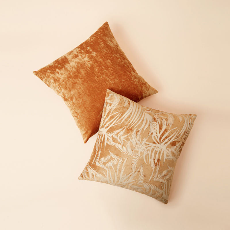 A pair of 18 * 18-inch Belinda yellow mustard velvet pillows with leafy motifs is exhibited in a staggered position.