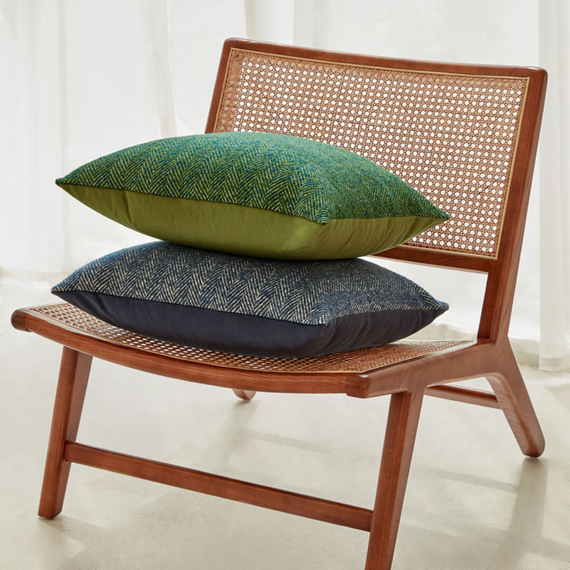 Two pillows in euro sham herringbone weave pillow cover is displayed on a bamboo chair. One is blue, the other is green.
