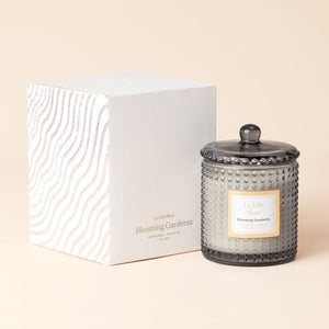 A glass jar of Blooming Gardenia candle with its white paper packing box.