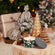 A burning candle and other Christmas ornaments are displayed on a small stump-like table.
