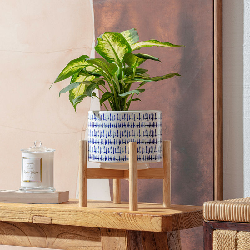 A China blue ceramic planter is placed on a wooden shelf with a white candle jar.