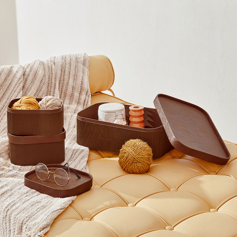A set of three brown baskets are placed on a light beige sofa bed. Two are stacked together with a large one beside.