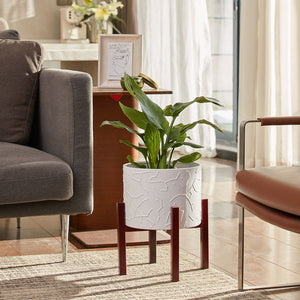 A white ceramic pot with sturdy stand is placed at the corner of two sofa, growing lush green plants.