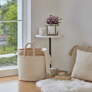 A laundry basket storing a large scarf is close to the window, next to a round white coffee table.
