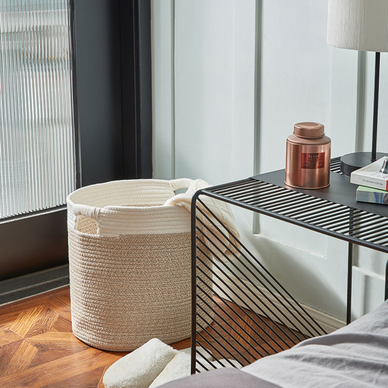 A cotton rope storage basket holding towels is placed between a transparent door and a metal coffee table.