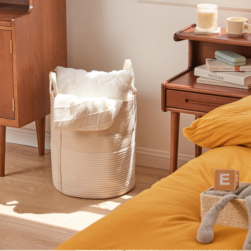 A cotton rope storage basket filled with cushions and blankets, is placed in between two bedside table.