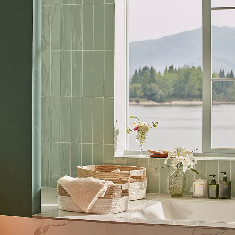 A full view of two cotton and jute storage baskets storing towels is displayed in a bathroom with a window background.
