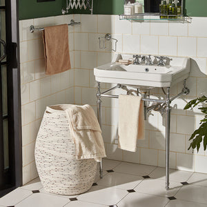 A towel is placed in a colored dots laundry basket in a bathroom. The hamper is placed against the white tile wall.