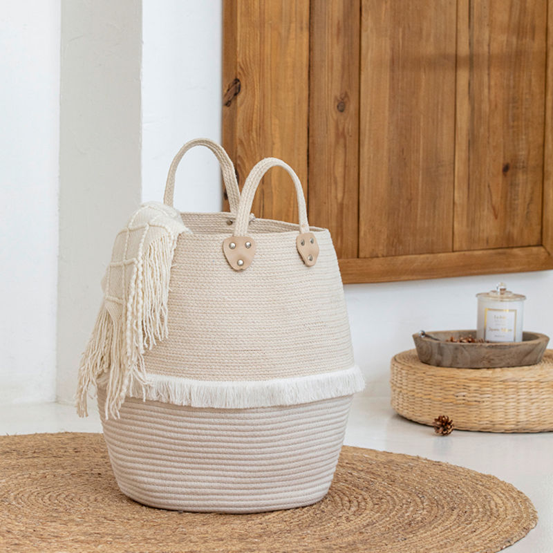 The beige laundry basket is filled with bed throws and blankets, placed on a mat and in front of a wooden tray.
