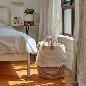 The laundry basket filled with bedding supplies is placed next to the bed, in the shadow of the window background.
