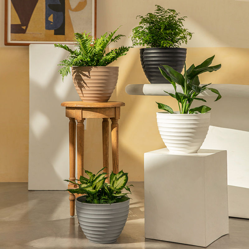 Four planter in different colors are displayed in a staggered way. The taupe pot is placed on a small wooden side table.