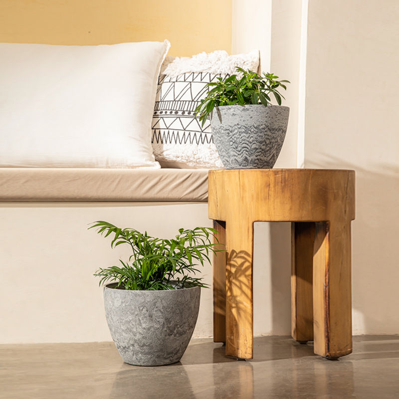 A set of two pots are displayed in front of a sofa. The large planter is placed on the ground and another pot stands on a wooden chair.